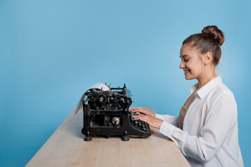 Naklejka premium young woman author at a typewriter, writes a text. A writer at a table with a vintage typewriter