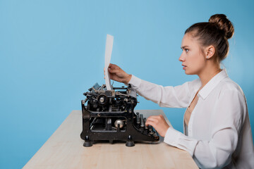 young woman writer at a typewriter looks at a piece of paper with surprise,