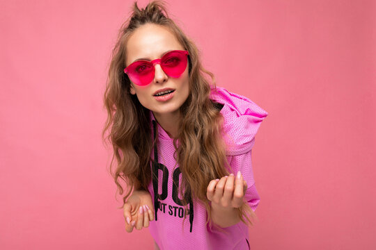 Photo shot of beautiful asking young dark blonde woman wearing casual clothes and stylish sunglasses isolated over colorful background looking at camera and having questions
