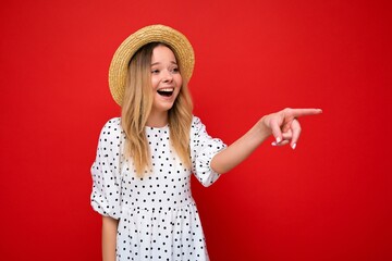 Portrait of beautiful fascinating emotional positive joyful happpy female promoter pointing to the side at copy space for advertising wearing hipster outfit isolated over background wall with empty