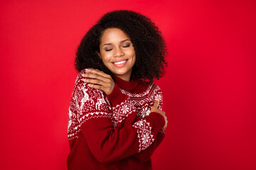 Portrait of attractive dreamy cheerful girl hugging herself wearing knitted jumper isolated over shine red color background