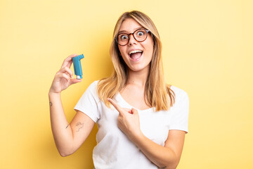 pretty blonde girl looking excited and surprised pointing to the side. asthma inhaler concept