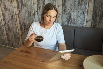 Charming pregnant woman drinks a drink and looks at the screen of a tablet.