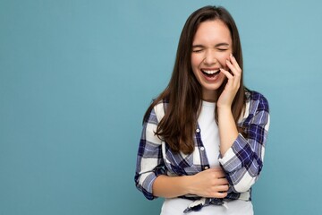 Photo portrait of young beautiful smiling hipster brunette woman in trendy blue and white shirt and jeans clothes. Sexy carefree female person posing isolated near blue wall with empty space in studio