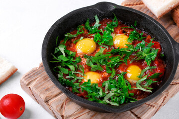 Shakshouka with quail eggs and tomato sauce topped with herbs served in cast iron pan. Middle Eastern and African meal