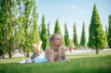 Attractive sportive girl lies on the grass and relaxes in park