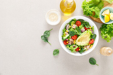 Avocado and tuna fresh vegetable salad with tomato, cucumber corn, onion, lettuce and spinach. Healthy and detox food concept. Ketogenic diet. Buddha bowl dish on light background, top view