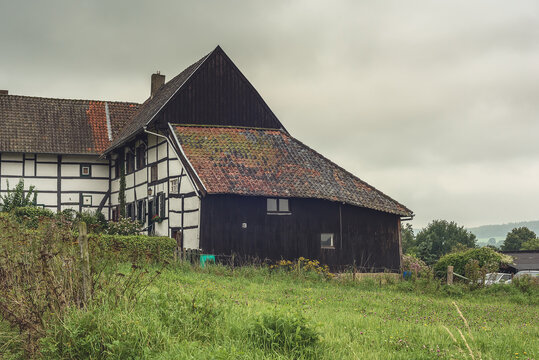 Old half-timbered farmhouse with wooden shed in a lush hilly landscape.