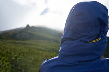 Man in blue hook is looking from the mountain. View from the back, close-up. Concept of lifestyle, vacation, tourism. Wild traveling and hiking in mountains