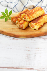 Delicious homemade fried or baked rolls made of wheat bread, sausage and cheese. Gourmet breakfast, brunch. Served on a wooden board with basil. White background. Selective focus, copy space