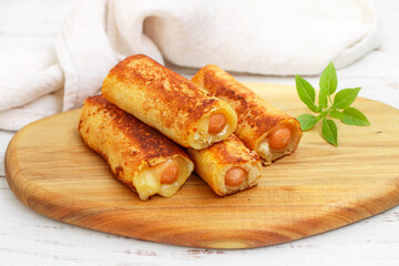 Delicious homemade fried or baked rolls made of wheat bread, sausage and cheese. Gourmet breakfast, brunch. Served on a wooden board with basil. White background. Selective focus, copy space