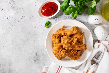 Fried crispy chicken legs in breadcrumbs in a white plate on a light culinary background. Fast food from the drumstick top view
