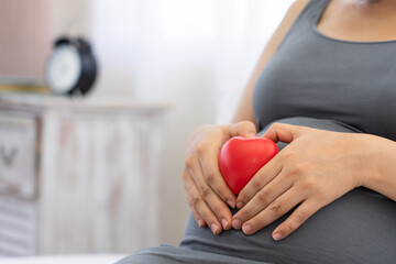 Pregnant woman holding red heart touching her belly. Loving mom waiting of a baby. Maternity,...