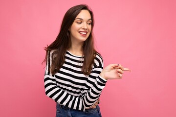 Portrait of beautiful fascinating emotional positive joyful happpy female promoter pointing to the side at copy space for advertising wearing hipster outfit isolated over background wall with empty