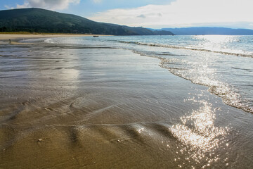Deserted beach with gentle waves on the sand and reflection of the sun in the water.
