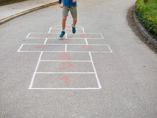 Young boy jumping and playing hopscotch, no faces shown