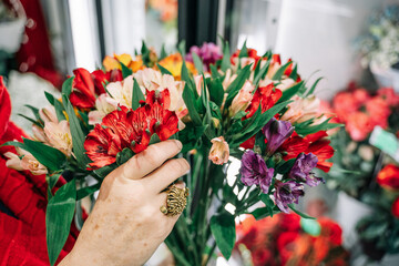 A florist woman with a red scarf, bracelets and a brass ring, holds alstroemeria flowers in her hand to assemble a bouquet. Flower show in the store.