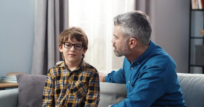 Dad and son of school age sit at home on couch and have serious conversation. Concept of disciplinary process in family.