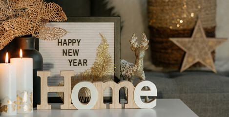 A sign with the inscription Happy New Year, a deer, a golden bouquet on the table and a beautiful bokeh in the background in the home interior of the living room. A cozy concept of a holiday and winte