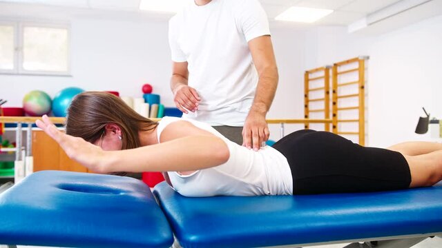Handheld shot of a Caucasian female patient and male physiotherapist during rehabilitation treatment. Woman lying on her abdomen, and doing extension stretch exercises for lumbar spine disc.