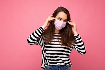 Young beautiful woman in reusable virus protective mask on face against coronavirus isolated on the pink background wall