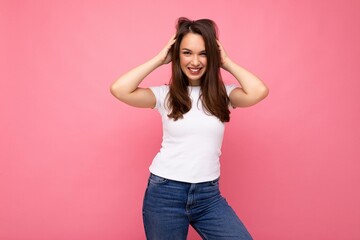 Photo portrait of young beautiful smiling hipster brunette woman in white t-shirt with mockup. Sexy carefree female person posing isolated near pink wall with empty space in studio. Positive model