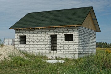 unfinished white private brick house with a green tiled roof in the grass against the sky