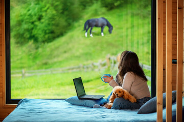 Woman sitting on the bed and looks outside the window seeing mountain. Concept of the workplace at...
