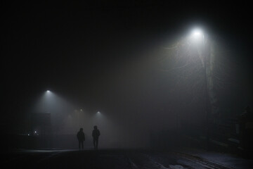 Urban winters scene of two men walking under street lights, foggy