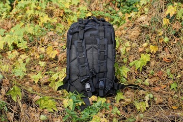 Fototapeta na wymiar one big black tactical backpack stand on dry gray vegetation with green leaves in nature