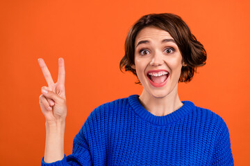Photo of cool brunette millennial lady show v-sign wear blue pullover isolated on orange color background