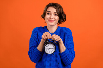Photo portrait woman smiling showing keeping alarm clock isolated vibrant orange color background copyspace