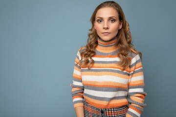 Young charming fascinating self-confident serious blond woman wearing casual striped pullover isolated over blue background with free space