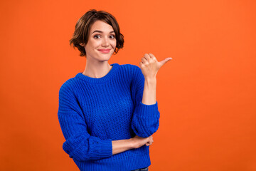 Photo of lovely brunette young lady point look empty space wear blue pullover isolated on orange color background