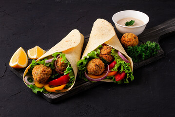 Tortillas wrapped with falafel balls and fresh vegetables, vegetarian healthy food, on a black...