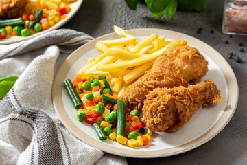 Fried crispy chicken legs in breadcrumbs with french fries and vegetables in a plate on a culinary background. Fast food from the drumstick close-up