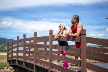 blonde lady and young brunette boy admiring the landscape over the bridge in sunny summer day, in the background blue sky with white clouds.