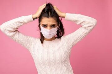 Young emotional woman wearing an anti virus protection mask to prevent others from corona COVID-19 and SARS cov 2 infection isolated over pink background