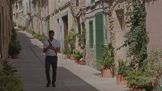 Hombre se hace un selfie con el m&oacute;vil en calle con casas estilo mediterr&aacute;neo  (Grabado en 6K con blackmagic RAW)