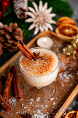 Obraz na płótnie Canvas A glass of traditional Christmas drink eggnog on a festive table, vertical photo. Spicy drink made from egg and milk with cinnamon, cardamom.