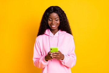 Photo portrait of african american girl holding phone in two hands isolated on vivid yellow colored background