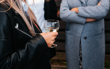 Woman with glass of white wine at festive outdoor event. Close-up of female hand holding alcoholic drink, selective focus