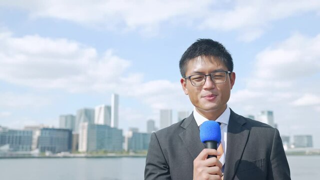都市を背景に話す男性レポーター