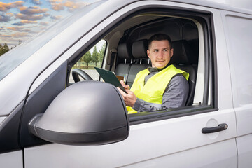 The driver plans to work on the tablet. Driver driving a cargo van. Satisfied man at work. Delivery of parcels. The postman chooses the delivery route. Concept of logistics services.