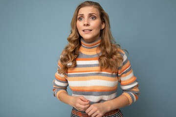 Obraz premium Photo portrait of young attractive beautiful sad upset touchy blonde woman with sincere emotions wearing striped pullover isolated on blue background with copy space and worries about