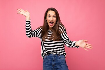 Photo of young emotional astonished shocked positive happy beautiful brunette woman with sincere emotions in casual striped pullover isolated on pink background with copy space