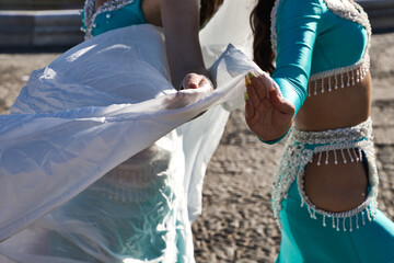 Detail of two young and beautiful belly dancers dancing in a square. They are dressed in light blue with white veils in their hands. World folklore concept from Africa and Asia.
