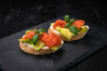 Bruschetta with salmon and avocado on a dark wooden table
