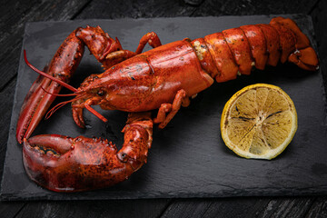 grilled lobster with lemon on a black slate board, on a dark wooden table
