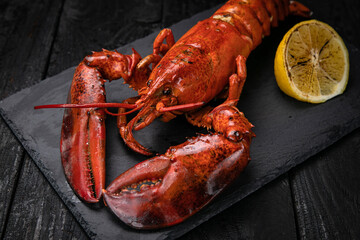 grilled lobster with lemon on a black slate board, on a dark wooden table
